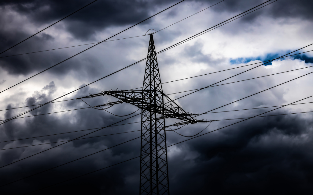 Transmission tower under storm clouds — situational awareness & weather resilience: icing detection, vibration monitoring, extreme-weather transparency (DLR brochure photography)